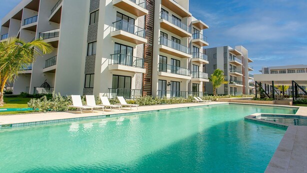 A modern hotel with a swimming pool, multiple balconies, and a well-maintained garden area. - First-floor apartment with pool view (Punta Cana)