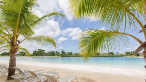 A beach with white lounge chairs and palm trees. - First-floor apartment with pool view (Punta Cana)