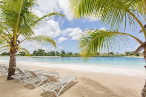 Ein Strand mit weißen Liegestühlen und Palmen.