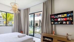 A modern hotel room with a large bed, a TV mounted on the wall displaying a movie selection, and a balcony with a view of the city. - First-floor apartment with pool view (Punta Cana)