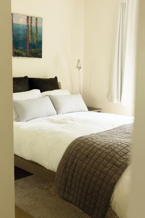 Ein Schlafzimmer mit einem Bett, Kissen, einem Nachttisch, einer Lampe und einem Bild an der Wand.