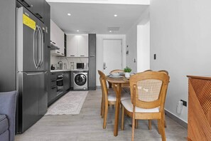 A modern kitchen with stainless steel appliances, a dining area with wooden chairs, and a grey floor. - New Luxury Condo | Pool View | Minutes to Beach (Punta Cana)