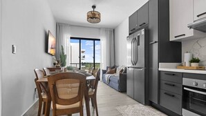 A modern kitchen with a built-in oven, a dining area with a table and chairs, and a sofa in the background. - New Luxury Condo | Pool View | Minutes to Beach (Punta Cana)