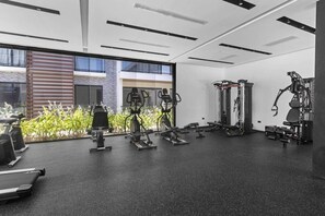 A modern gym with various exercise equipment, large windows, and a view of the outside. - New Luxury Condo | Pool View | Minutes to Beach (Punta Cana)