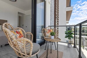A balcony with wicker chairs, a small table, and potted plants. - New Luxury Condo | Pool View | Minutes to Beach (Punta Cana)
