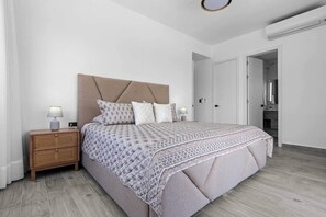 Un dormitorio con cama, mesitas de noche y una puerta que da a otra habitación.