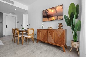 A dining area with a wooden table and chairs, a decorative cabinet, and a large potted plant. - New Luxury Condo | Pool View | Minutes to Beach (Punta Cana)