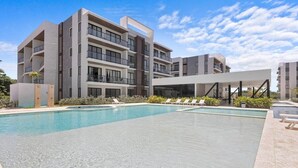 A modern building with a swimming pool and lounge chairs. - New Luxury Condo | Pool View | Minutes to Beach (Punta Cana)