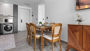 A modern kitchen with a washing machine, a dining area with a round table and chairs, and a decorative cabinet. - New Luxury Condo | Pool View | Minutes to Beach (Punta Cana)
