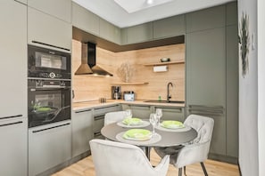 Eine moderne Küche mit integrierten Geräten, ein Essbereich mit rundem Tisch und Stühlen sowie eine Wand als Holzakzent.