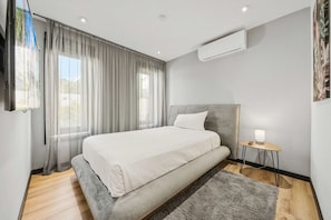 Ein Schlafzimmer mit Bett, Nachttisch mit Lampe, Klimaanlage und Fenster mit Vorhängen.