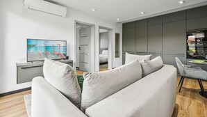 Ett modernt vardagsrum med en soffa, en platt-TV och en matplats med ett bord och stolar.