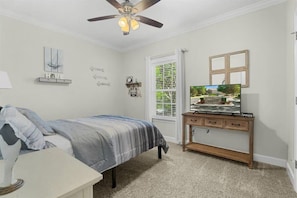 A bedroom with a bed, a TV on a wooden stand, a ceiling fan, and a window with blinds. - Stunning 3BR, 2BA luxury retreat with pool view, just 7 miles from the beach! (Foley)