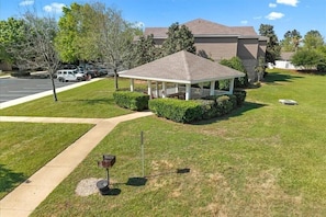 A gazebo with a white railing, surrounded by well-maintained grass and bushes, near a building with a brown roof. - Stunning 3BR, 2BA luxury retreat with pool view, just 7 miles from the beach! (Foley)