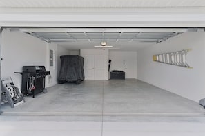 A clean, empty garage with a covered vehicle, a workbench, and a ladder. - Bright & Pet-Friendly Cottage Home in the Village of Well Point (Sumterville)