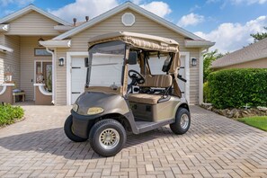 Ein Golfwagen vor einem Haus mit Garage, Auffahrt und Hecke.