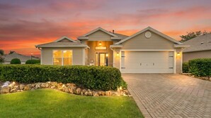 A residential house with a garage, a well-maintained lawn, and a stone wall. - 3/2 Designer in Village of Mallory Square Dog friendly w/ Golf cart (The Villages)