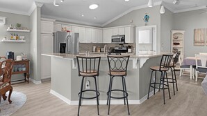 A modern kitchen with a central island, bar stools, and a dining area with a table and chairs. - 3/2 Designer in Village of Mallory Square Dog friendly w/ Golf cart (The Villages)
