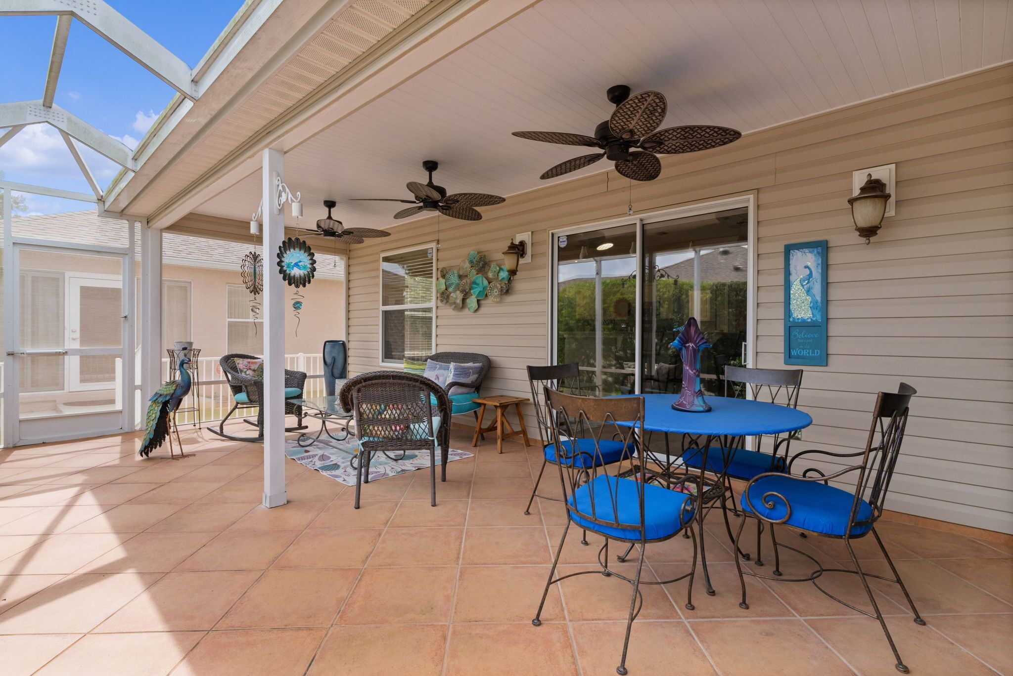 A covered patio area with ceiling fans, outdoor seating, and a decorative peacock statue.