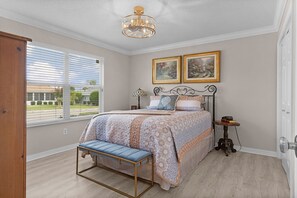 Ein Schlafzimmer mit einem Bett, einer Bank, einem Nachttisch, einer Lampe und zwei gerahmten Bildern an der Wand.