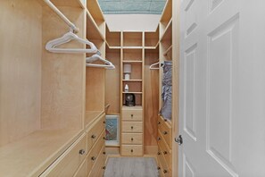 Ein begehbarer Kleiderschrank mit Holzböden, einem ausklappbaren Stuhl in der Mitte und einer weißen Tür.