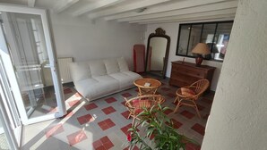 Ein Zimmer mit einer Couch, zwei Korbstühlen, einem kleinen Tisch, einem Spiegel und einer Kommode.