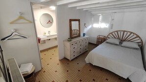 Ein Schlafzimmer mit einem Bett, einem Schminktisch, einem Spiegel, einem Sessel und einem Badezimmer mit Waschbecken und Toilette.