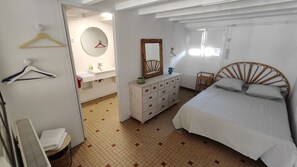 Ein Schlafzimmer mit einem Bett, einem Schminktisch, einem Spiegel, einem Sessel und einem Badezimmer mit Waschbecken und Toilette.