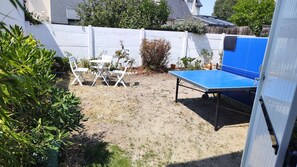 Ein Garten mit Tischtennisplatte, weißen Stühlen und einem kleinen Gartenbereich.
