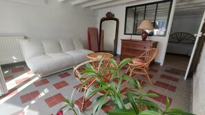 A room with a white sofa, a round wicker table, a dresser, and a mirror. - Garden level 300m from the Nau beach (Le Pouliguen)