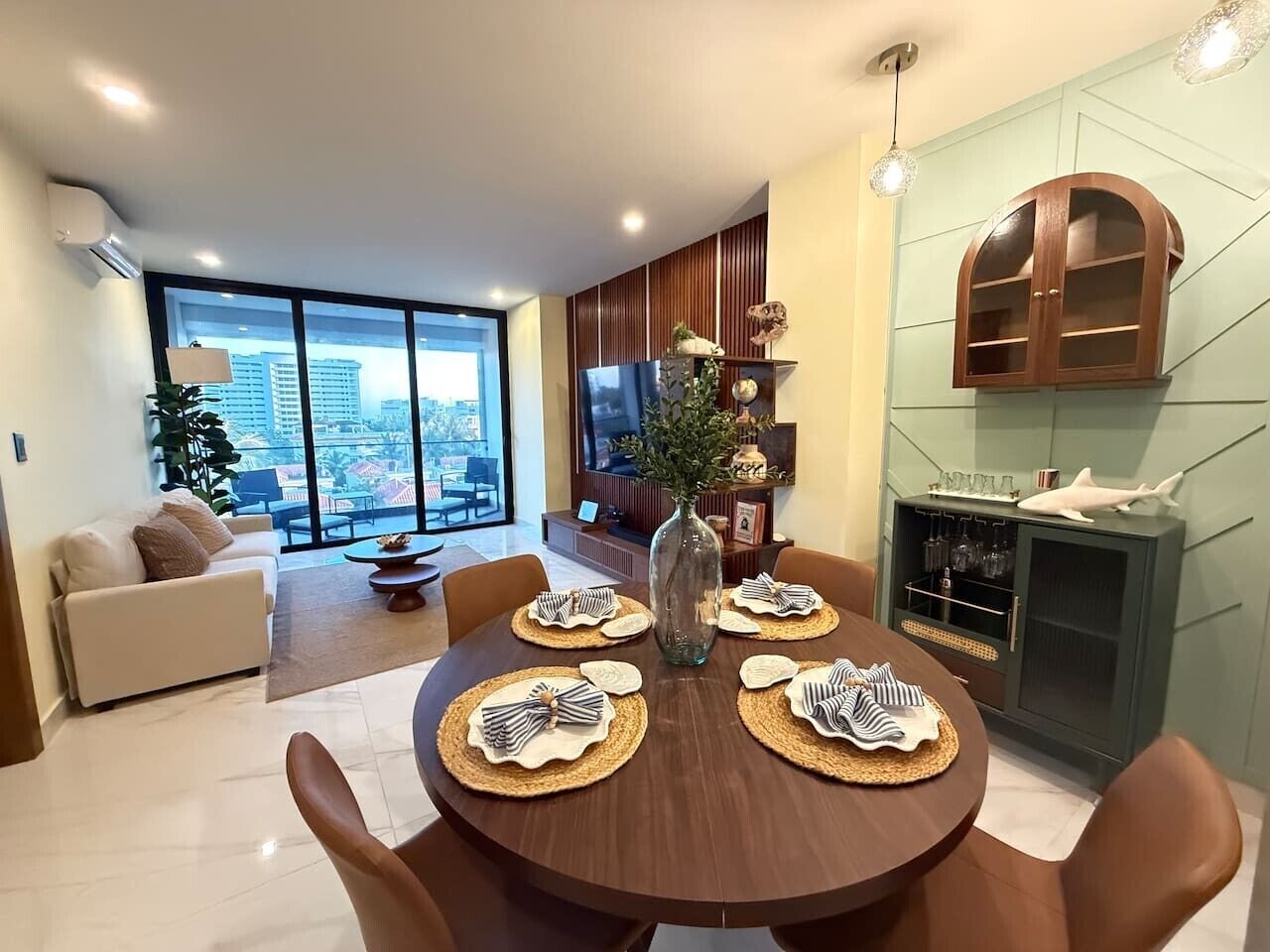 A modern dining area with a round table set for four, a vase centerpiece, and a city view through large windows.
