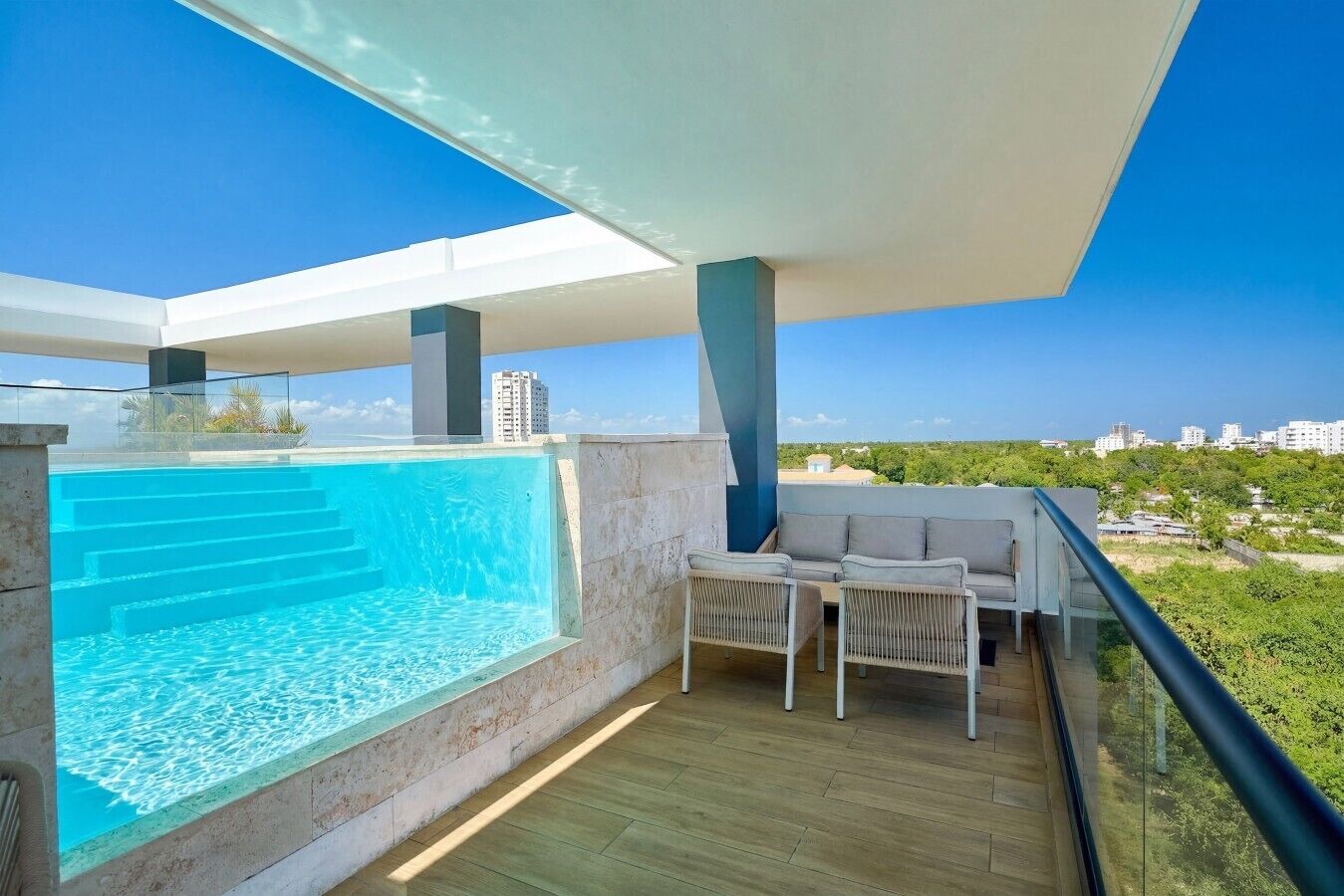A modern balcony with a built-in swimming pool, a seating area with a sofa and chairs, and a clear view of the surrounding landscape.
