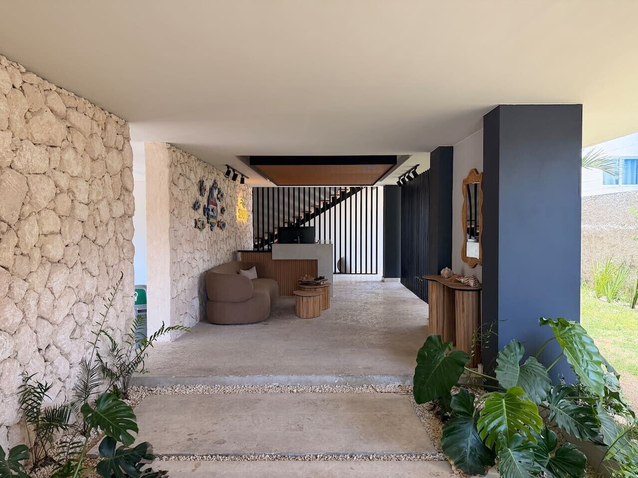 Un intérieur moderne avec un mur en pierre, un escalier, un coin salon avec un fauteuil poire et une grande plante.