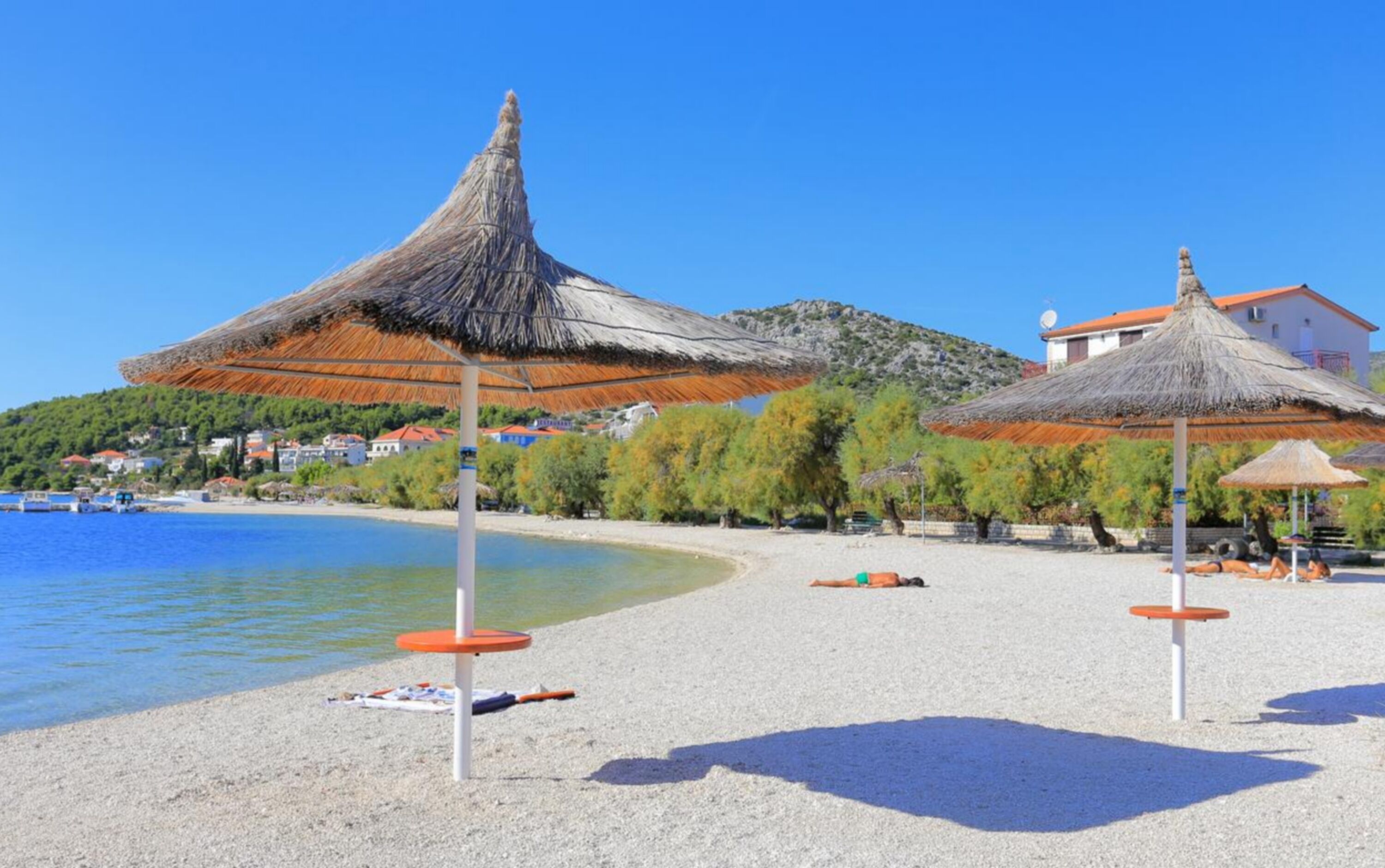 A beach with thatched umbrellas and a clear blue sky.