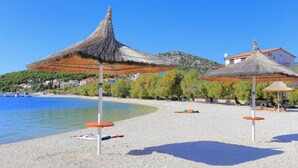 Une plage avec des parasols en chaume et un ciel bleu dégagé.