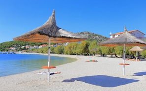 A beach with thatched umbrellas and a clear blue sky.