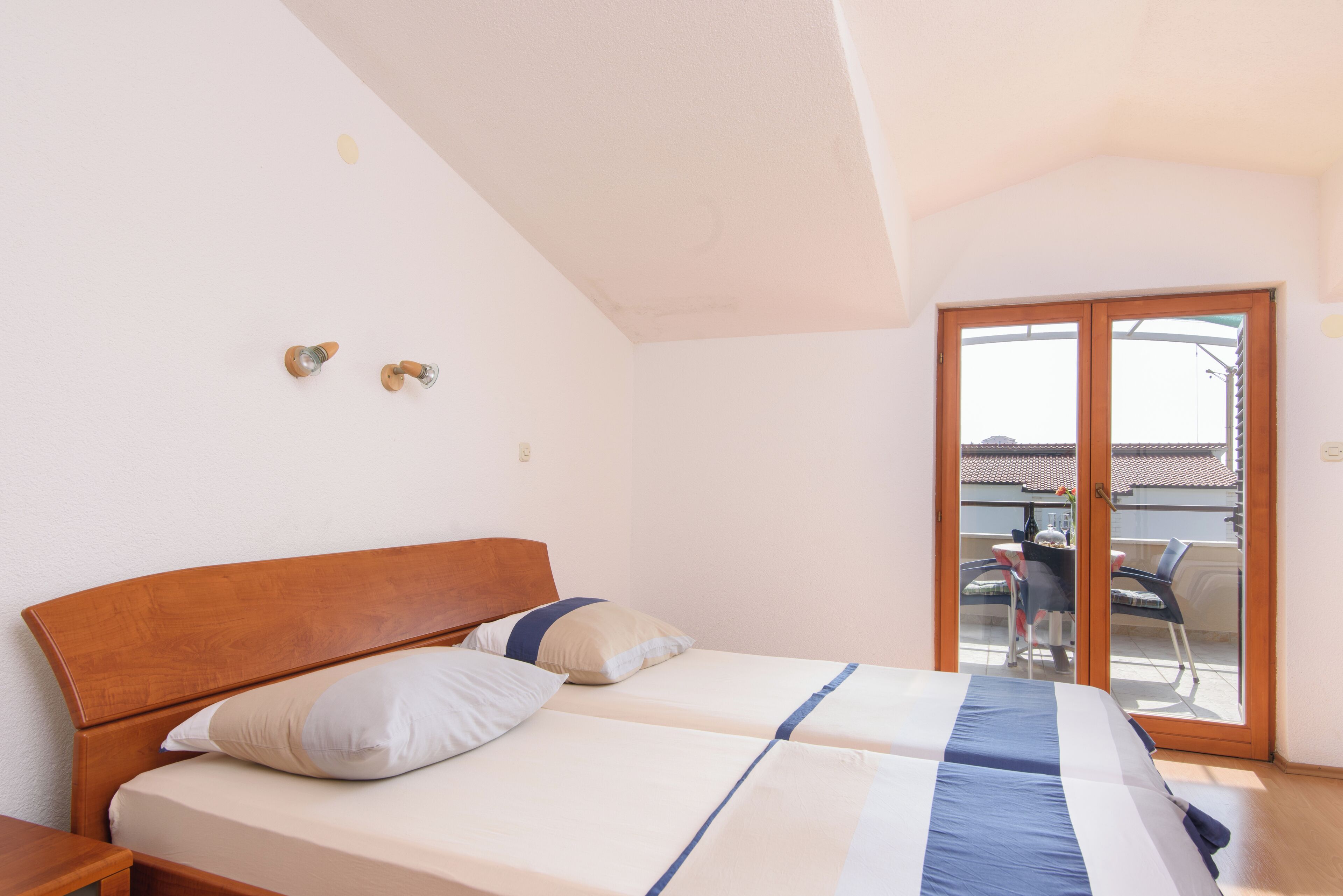 Een slaapkamer met een houten bed, twee kussens, een nachtkastje en een schuifdeur naar een buitenruimte.