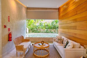 A room with a sofa, a chair, a round table, and a view of a garden with a pool. - FrontBeach Apt Pool AC Juan Dolio Beach Aquarella (Playa Juan Dolio)