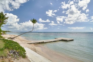 A beach with a wooden dock extending into calm waters, surrounded by greenery and a clear sky. - FrontBeach Apt Pool AC Juan Dolio Beach Aquarella (Playa Juan Dolio)
