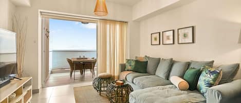 Ein modernes Wohnzimmer mit Sofa, Fernseher, Esstisch und Meerblick.