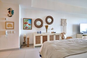 A hotel room with a bed, a desk, a television, a decorative wall, and a painting. - FrontBeach Apt Pool AC Juan Dolio Beach Aquarella (Playa Juan Dolio)
