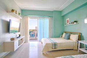 A bedroom with a bed, a TV, a desk, and a balcony with a view. - Tropical BeachSide Apartment 4PAX AC La Velas (Playa Juan Dolio)