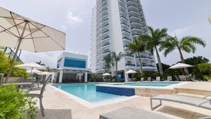 Ein Hotel mit Poolbereich, Palmen und einem hohen Gebäude im Hintergrund.