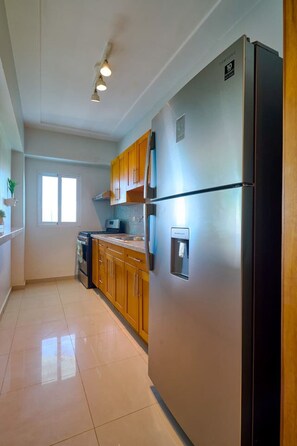 A kitchen with stainless steel appliances, wooden cabinets, and a tiled floor. - Tropical BeachSide Apartment 4PAX AC La Velas (Playa Juan Dolio)