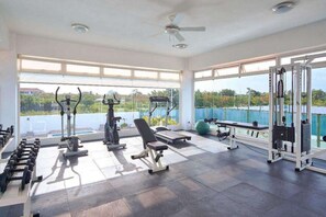 A gym with various exercise equipment, large windows, and a view of greenery. - Tropical BeachSide Apartment 4PAX AC La Velas (Playa Juan Dolio)