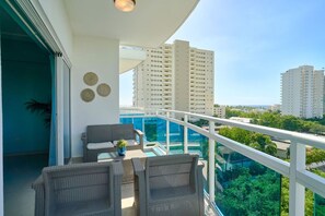 Un balcon offrant une vue sur de hauts immeubles, une piscine à débordement et des meubles d’extérieur.