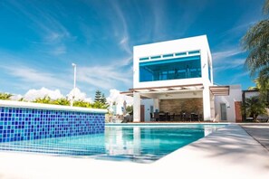 Un bâtiment moderne doté d’une piscine, d’un espace extérieur aménagé et surplombant un ciel d’un bleu éclatant.