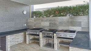 A modern outdoor kitchen with three gas stoves, a built-in grill, and a stone-textured backsplash. - Caribbean BeachSide Apt Juan Dolio Beach Las Velas (Playa Juan Dolio)