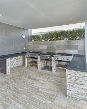 Eine moderne Außenküche mit drei Gasherden, einem integrierten Grill und einer Rückwand mit Steinoptik.