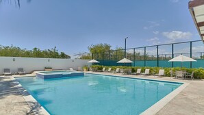 A rectangular swimming pool with a tiled edge, surrounded by lounge chairs and umbrellas, and a fence enclosing the area. - Caribbean BeachSide Apt Juan Dolio Beach Las Velas (Playa Juan Dolio)